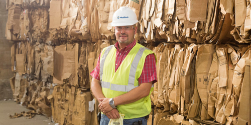 A man in a vest and hard hat standing in front of recycled fiber paperboard.