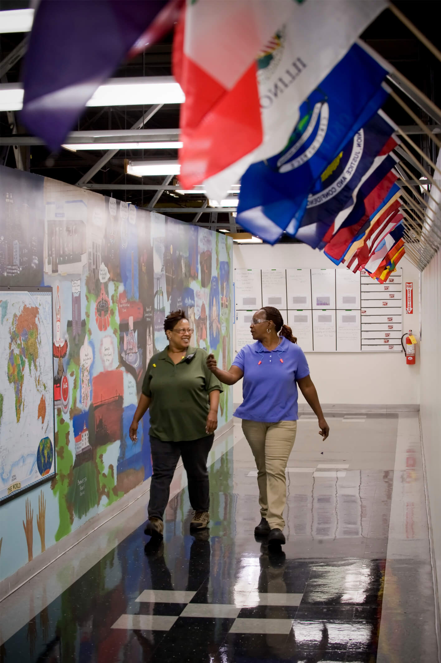 Two women walking down a hallway with national flags hanging from the wall.