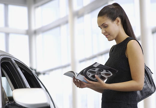 Une femme debout à côté d’une voiture lisant une brochure