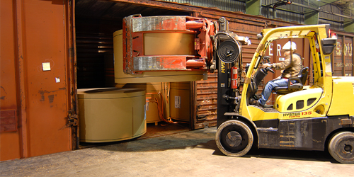 A forklift loading a roll of paperboard into a shipping crate.