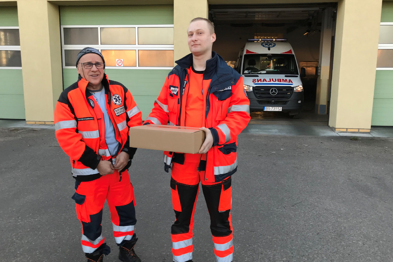 Dois homens com uniformes de socorristas segurando uma caixa