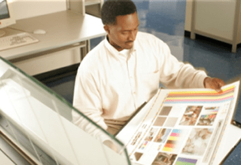 A man in an office looking at printing specifications on a large sheet of paper.