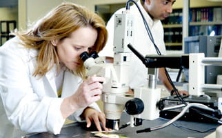 Uma mulher em um laboratório olhando em um microscópio.