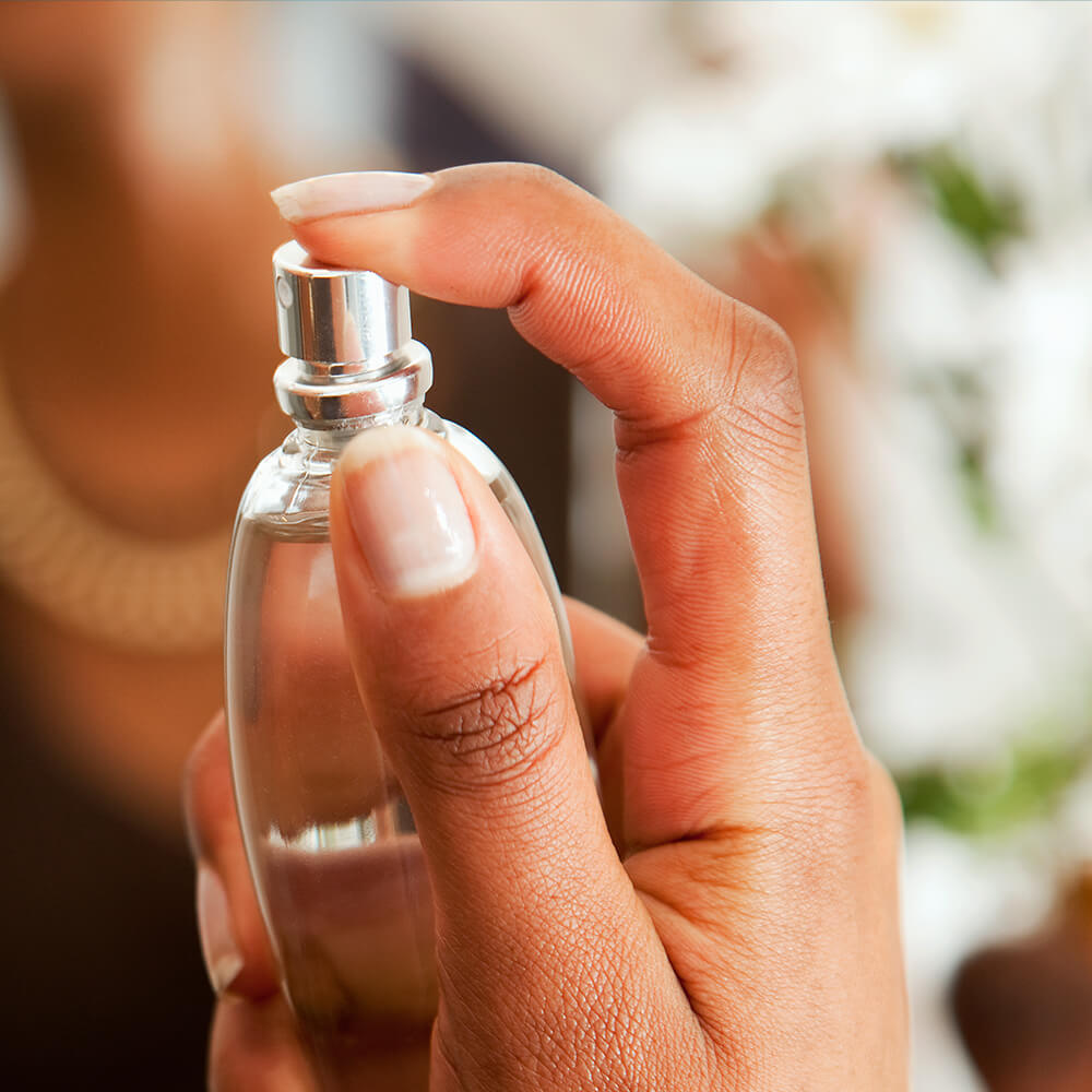 A woman holding up a perfume bottle with her hand.