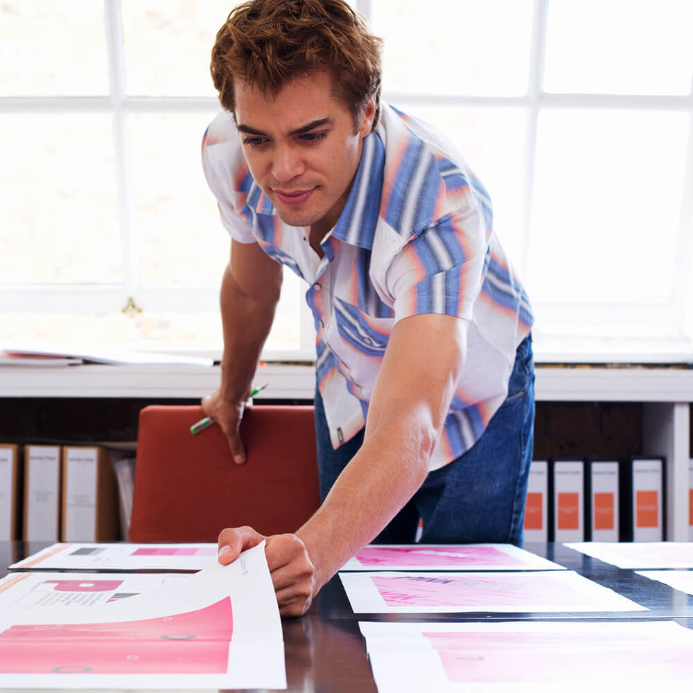 A man reviewing graphic design prints in an office.