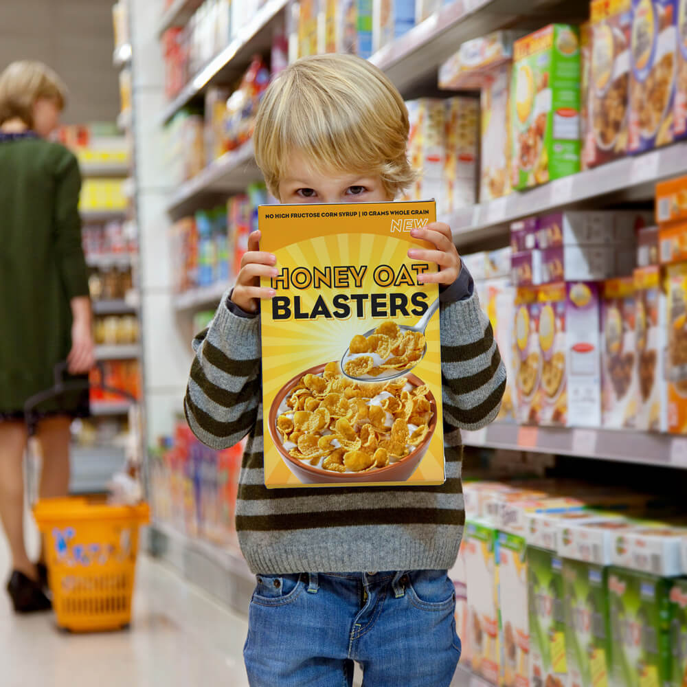 Um menino de pé em uma mercearia com uma caixa de cereal cobrindo o rosto.