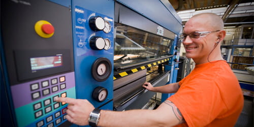 A man in an orange shirt preparing a piece of machinery for use.