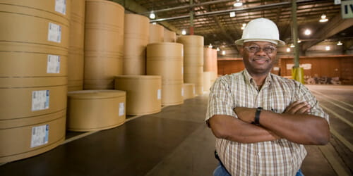 A man with his arms folded standing in front of paper rolls.