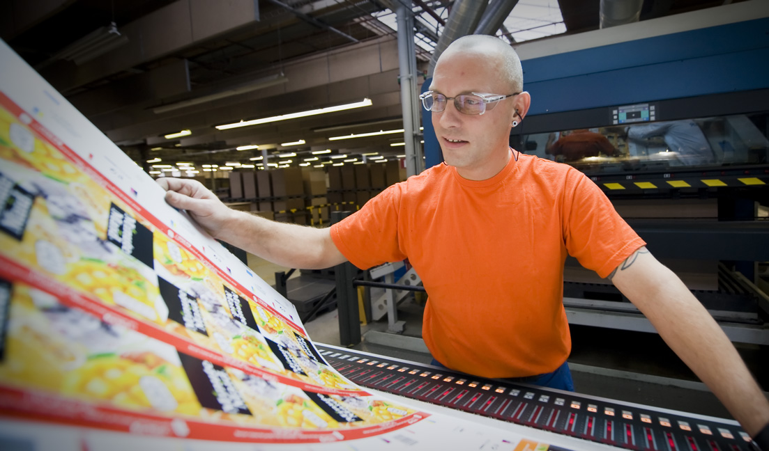 A man in orange shirt looking over commercial printing sheets at a manufacturing facility